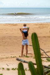 Mulher com filho em seus ombros, na praia, olhando o mar, Guarapari, ES, Brasil.