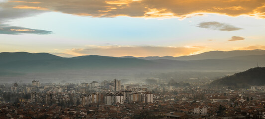 Fototapeta na wymiar Amazing panorama of Pirot cityscape during golden hour with dramatic, burning clouds in the sky and soft light on the town