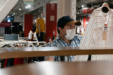 man in medical mask looking at clothes for purchase