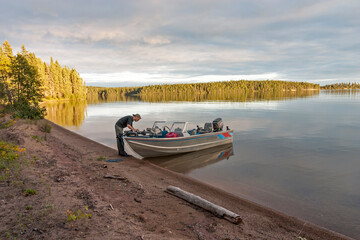 Fototapeta premium Fisherman tends to his boat on a serene lake in the Canadian North.