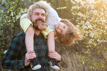 Happy child with father in spring park. Happy dad and son. Fathers day. Shoulder ride. Summer on...