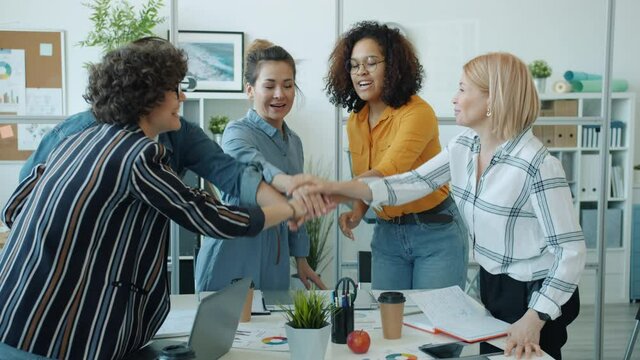 Diverse group of cheerful women are joining hands then applauding and doing high-five gesture in office. Successful work and community concept.