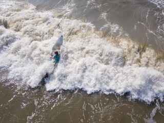 Aerial view of teen boy on a surfboard going out into the ocean.