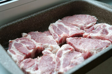 Raw pieces of pork laid in a bowl for further baking in the oven. In the kitchen.
