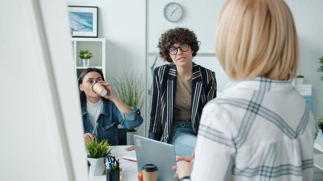 Group of smart cheerful women talking to speaker making presentation in office pointing at board sharing ideas. Business activity and conversation concept.