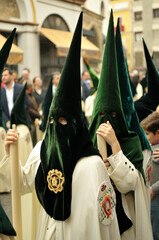 Nazarenos con túnica verde y cirios blancos de una hermandad de la Semana Santa de Sevilla (Andalucía, España). - obrazy, fototapety, plakaty