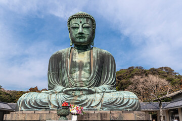 The Great Buddha, Daibutsu, offerings in front, blue sky above in Kamakura, Japan