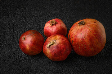 One large ripe pomegranate fruit with three small pomegranate fruits on a dark background texture.