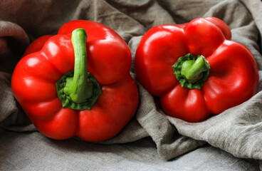 Two large red peppers lie on a linen tablecloth, like ingredients for a Mexican stew.