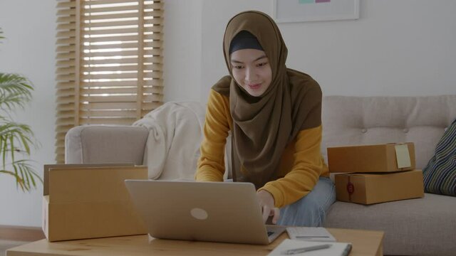 Muslim young women wear hijab using typing and checking order the customer address on the computer laptop at home morning. Concept business small and shop online