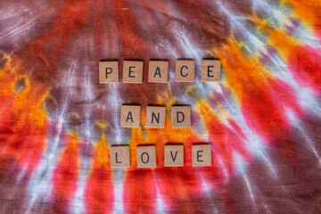 Peace and Love spelled out in wooden letters on a hippie-style burst pattern tie dye textile background. February 2021. 