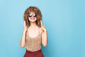 Attractive woman Fun curly hair hands near face blue background brown pants 