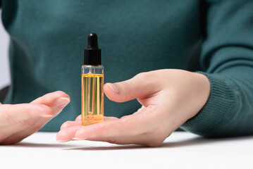 Woman is showing a bottle of cuticle oil close up. Finger nail care.