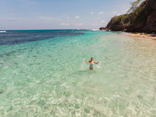 Obraz na płótnie Canvas Drone aerial view happy woman enjoying on beach with amazing clear turquoise water stand in the sea with open arms