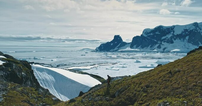 Tourist hiking Antarctica green rock mountain hill down. Ice and snow covered island at hill down. Landscape of polar winter nature at environment preserve scenery. Traveler expedition to South pole