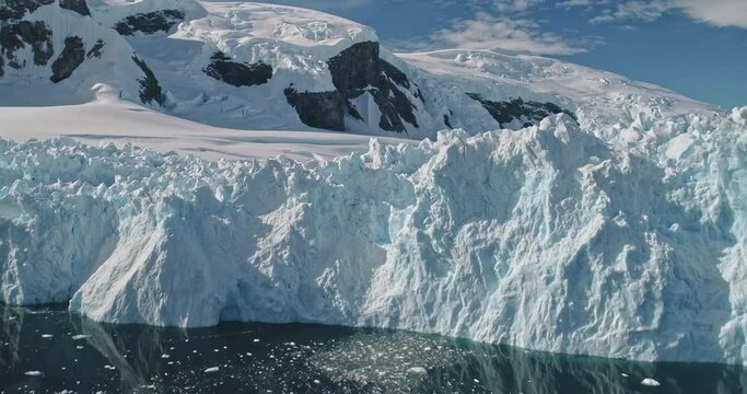 Mountain glacier with snow and ice at ocean bay aerial. White icy and snowy desert nature seascape at frozen dark blue water. Melting icebergs and climate change scenery. Epic arctic winter landscape