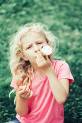 Cute funny adorable girl with long blonde messy hair eating licking ice cream from waffle cone. Child eating tasty sweet cold summer food outdoors. Summer frozen meal snack.