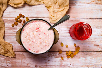 A cup of oatmeal with strawberries, raisins and strawberry jam on a wooden table. Delicious and healthy food for children at home.