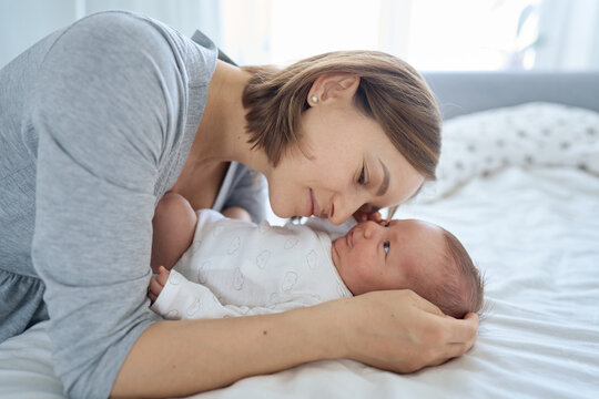 Close up of cute one months old baby boy lying on bed and playing with his Mum. Mum talking to son and cuddling him. High quality photo