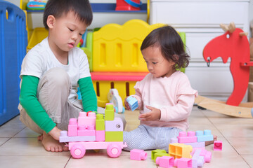 Asian cute big brother and little sister having fun playing with toy blocks in play room at home,...