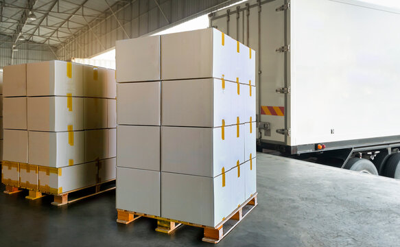Stack of cardboard boxes on pallet rack load into shipping container. cargo shipment boxes. trailer parked at loading dock warehouse. industry freight truck transportation.