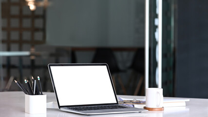 Computer laptop with blank screen, coffee cup and office supplies on office desk.