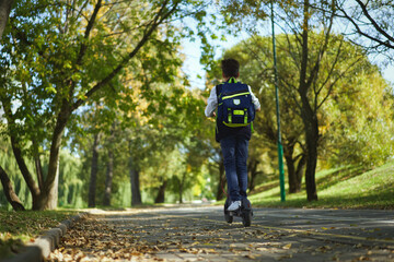 Schoolboy with backpack riding on electric scooter to school