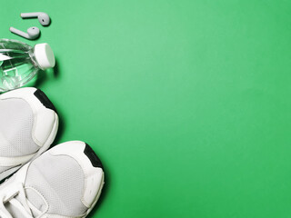 Healthy life concept. Top view on green background with sport shoes, water bottle and earbuds. 