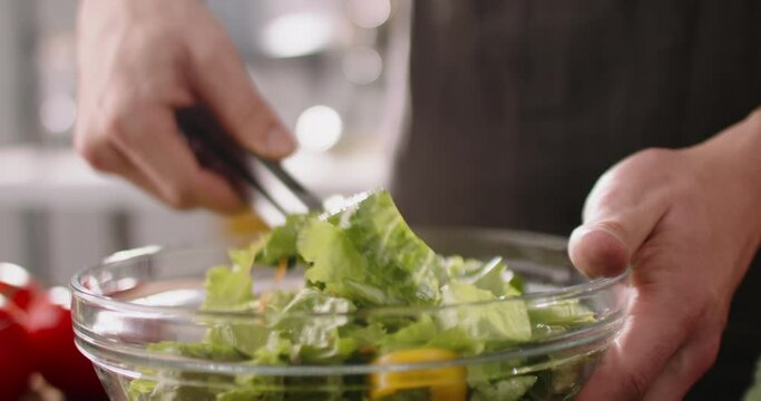 Close up shot of chef mixing healthy green salad in a bowl. Cooker cooking healthy vegetarian meal, 4k footage