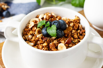 Homemade granola made from buckwheat. Organic buckwheat granola, green buckwheat sprouts, hazelnuts, pumpkin seeds, flax seeds and nutmeg. Granola in a white plate on the light gray kitchen table