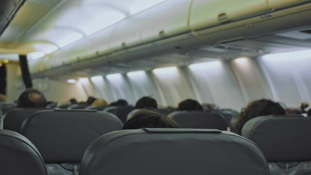 Airplane seats filled with passengers. Shot of an airplane cabin. the seats in the passenger plane are filled with passengers. Passengers are sitting. Above them are hand luggage compartments