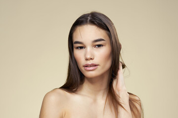 Fototapeta premium Brunette with bare shoulders close-up long hair beige background clean skin