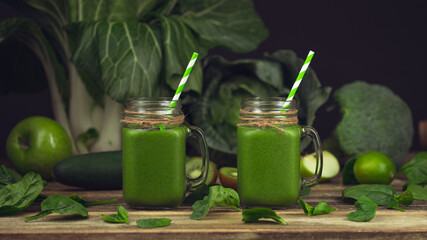 Green smoothie with ingredients on wooden table. Blended Spinach, Kale, kiwi, green Granny Smith apple, lime, broccoli Glass jar. Mason Jar with handle for drinking smoothie with green striped straw.