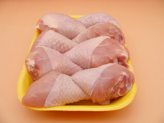 Fresh raw chicken shin meat in a yellow tray on a beige background.