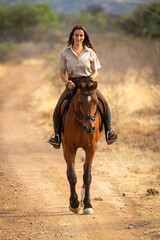 Smiling brunette rides horse along dirt track