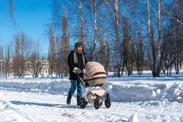 Fototapeta na wymiar Tired father walking with baby carriage in winter park