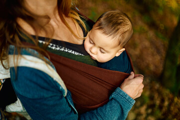 Young mother in the woods with her baby in sling on autumn day