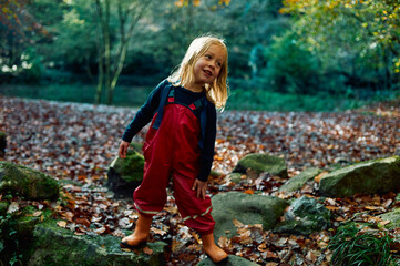 Preschooler in waterproof clothing playing in the woods on an autumn day