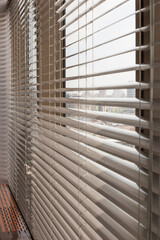 Aluminum blinds on the office windows. Made from metal. Venetian blinds closeup on the window. Silver color. City landscape is in the background. Modern sun protection and window decoration. Selective