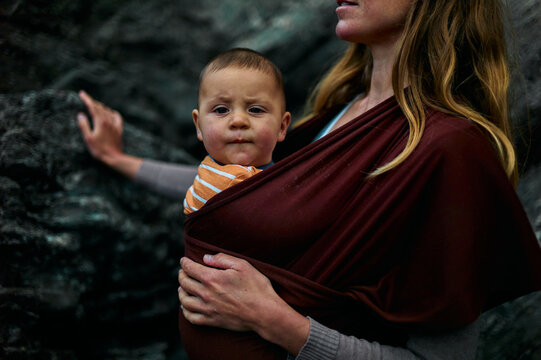 Young mother with baby in sling walking outdoors in autumn