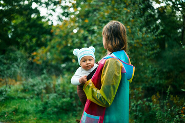 Young mother in forest with her baby in a sling on an autumn day