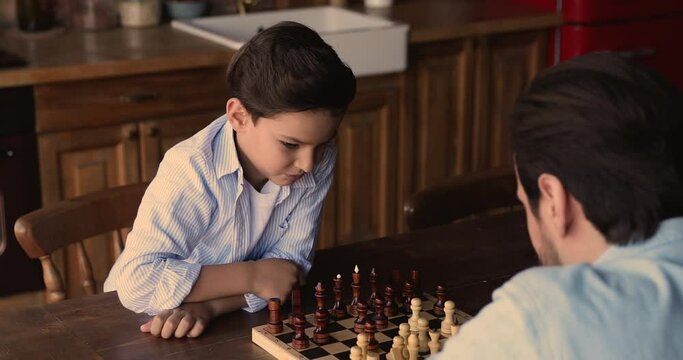 Smart focused little boy moving chess, playing with young father, enjoying domestic leisure hobby activity, improving logic skills, training memory or strategy view, entertaining together at home.