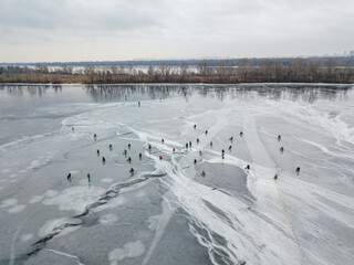 Fototapeta na wymiar Fishermen on thin ice. Frosty drawing on ice. Aerial drone view. Winter cloudy morning.