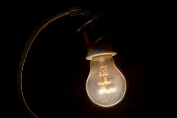An old lamp with a glowing light bulb on a black background