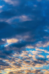 Dramatic clouds in blue sky, illuminated by rays of sun at colorful sunset to change weather. Soft focus, motion blur summer cloudscape background.