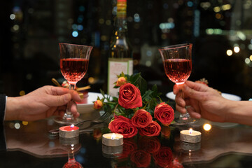 rose flowers and candles in table setting. Hands holding wine and blurred colorful city night in background