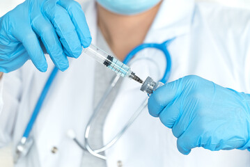 Close up of female doctors hands in medical gloves fills syringe with drug on background of white...