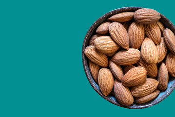 Almonds in a bowl isolated on teal background. Copy space. Healthy snack. Flat lay. 