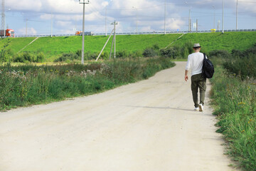 Fototapeta na wymiar A man walks along a country road. Hitchhiker around the country. A man stops a passing car on the road.