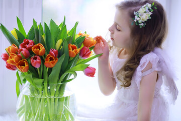 Beautiful girl in white dresses with a magnificent bouquet of the first tulips. International Women's Day. Girl with tulips.